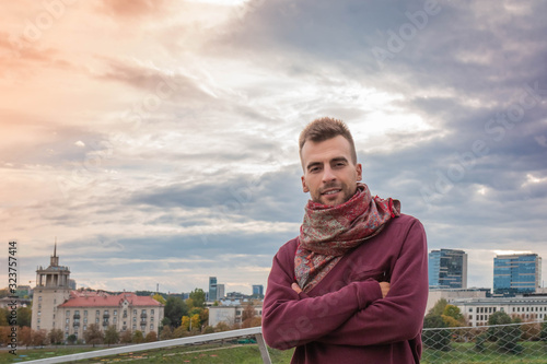 Young man with crossed arms at dramatic sky and urban background