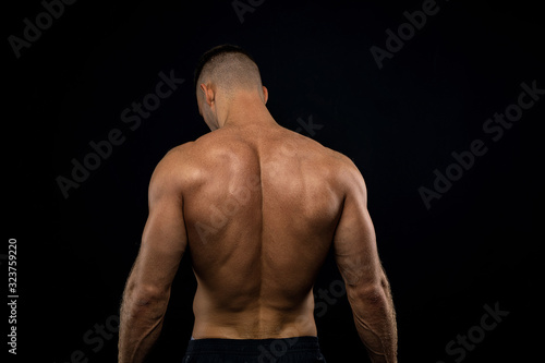powerful muscular athlete shows off his back beside black wall