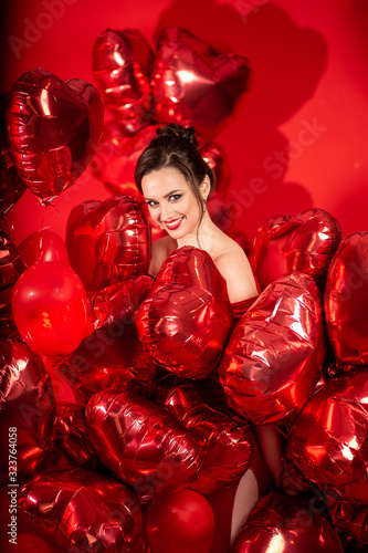Beautiful young woman in red evening dress posing over red background with big heart shape balloons.  © cherry_d