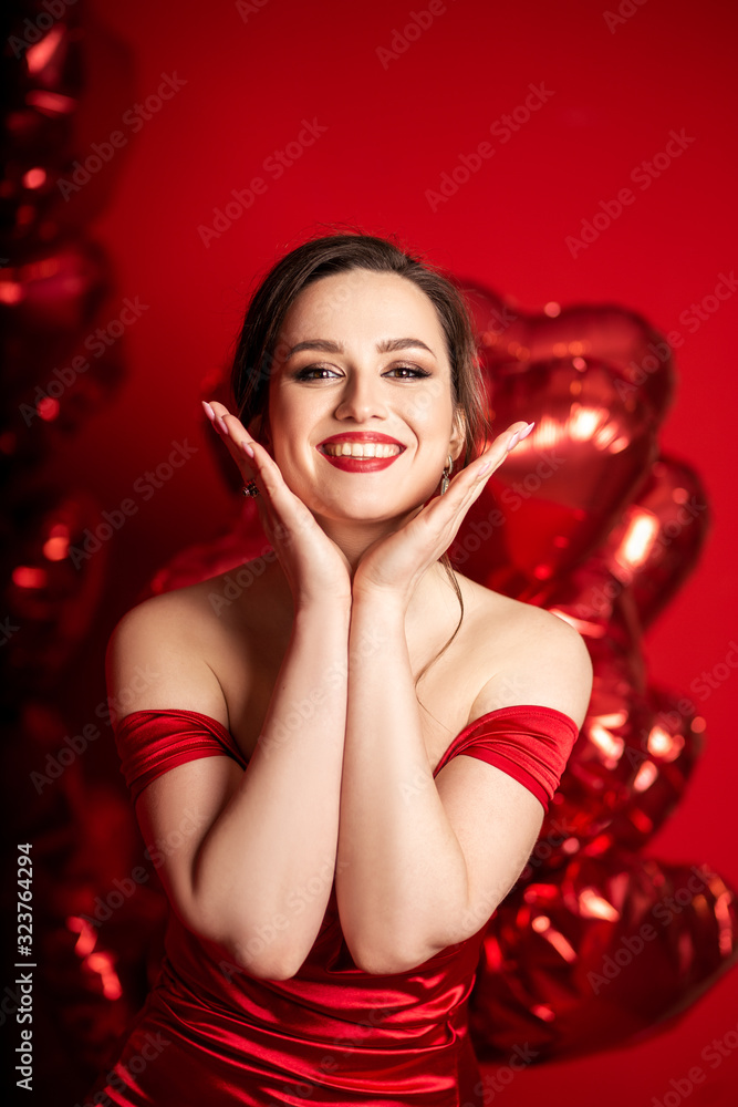 Beautiful young woman in red evening dress posing over red background with big heart shape balloons. Beautiful young woman in red evening dress posing over red background with big heart shape balloons.