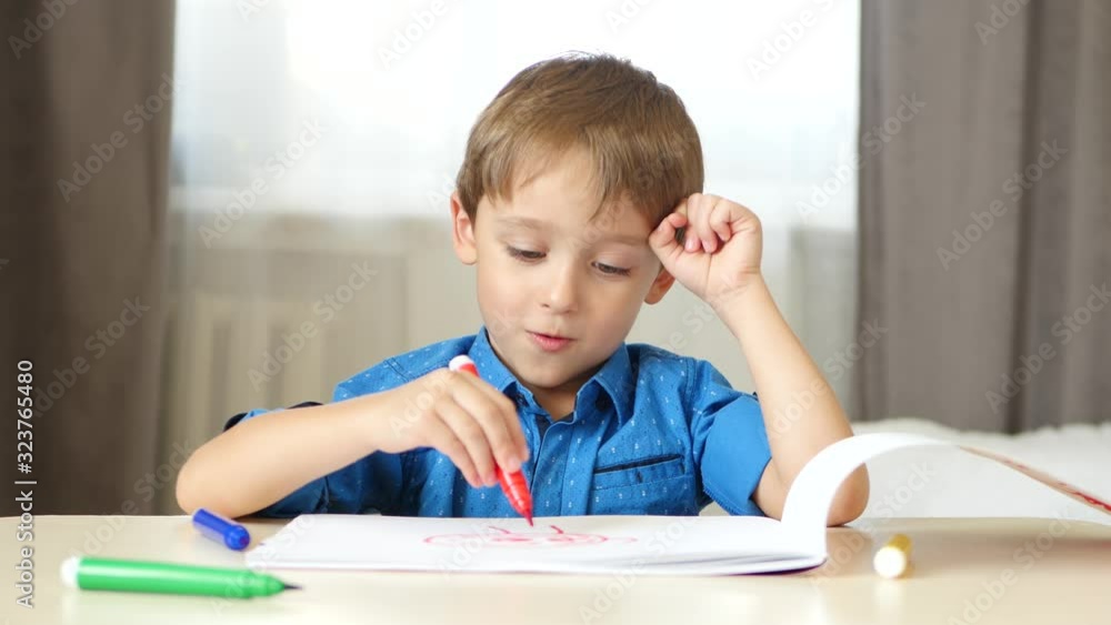 A little caucasian boy spends time drawing with colored pencils while sitting at a table. The child experiences emotions of joy and happiness. Lifestyle. A little caucasian boy spends time drawing with colored pencils while sitting at a table. The child experiences emotions of joy and happiness. Lifestyle.
