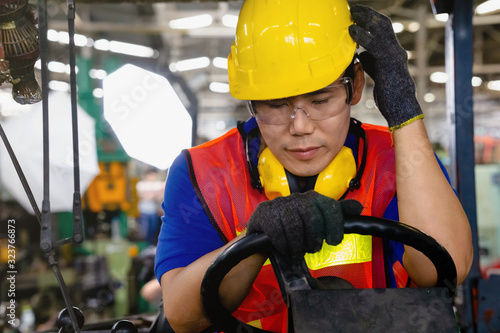 A worker with yellow safety helmet and goggles driving a forklift or reach  truck having a strong headache or sick at the logistics warehouse store.