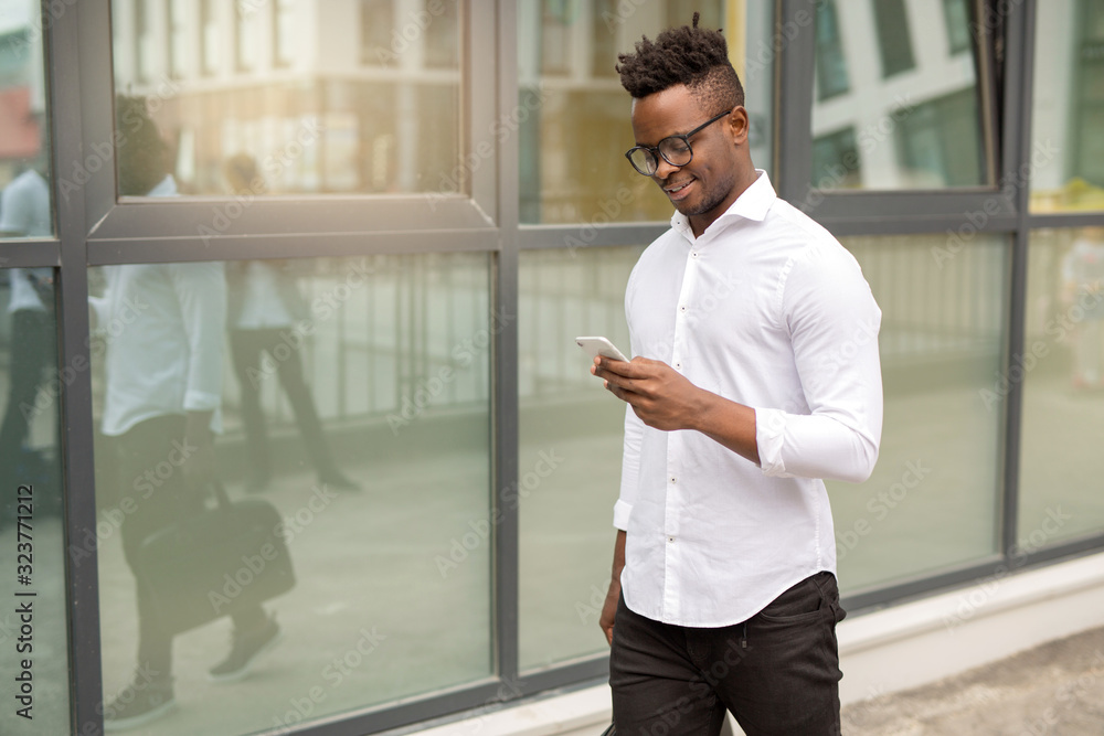 handsome young african man in a white shirt with a phone in his hands near a glass building handsome young african man in a white shirt with a phone in his hands near a glass building