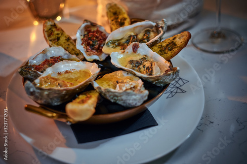 Tasty dinner golden metallic bowl of prepared oysters and crispy bread loafs with sauce and vegetable spread served on a white stone table next to candle, jellyfish in a glass stone decoration, wine