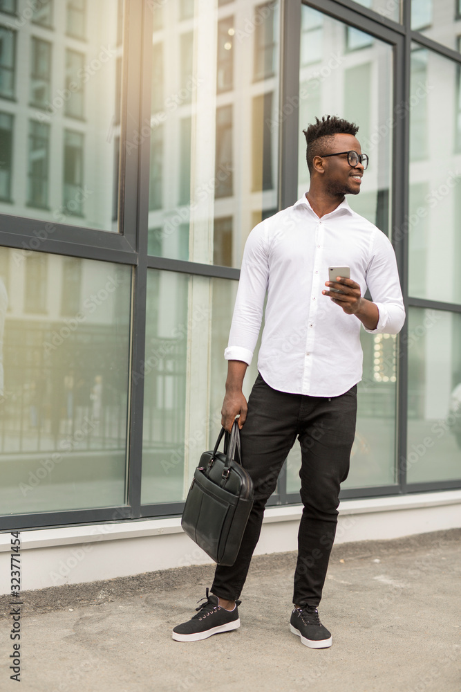 handsome young african man in a white shirt with a phone in his hands near a glass building handsome young african man in a white shirt with a phone in his hands near a glass building