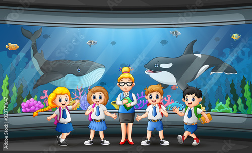 Group of kids watching fishes at aquarium excursion with woman teacher