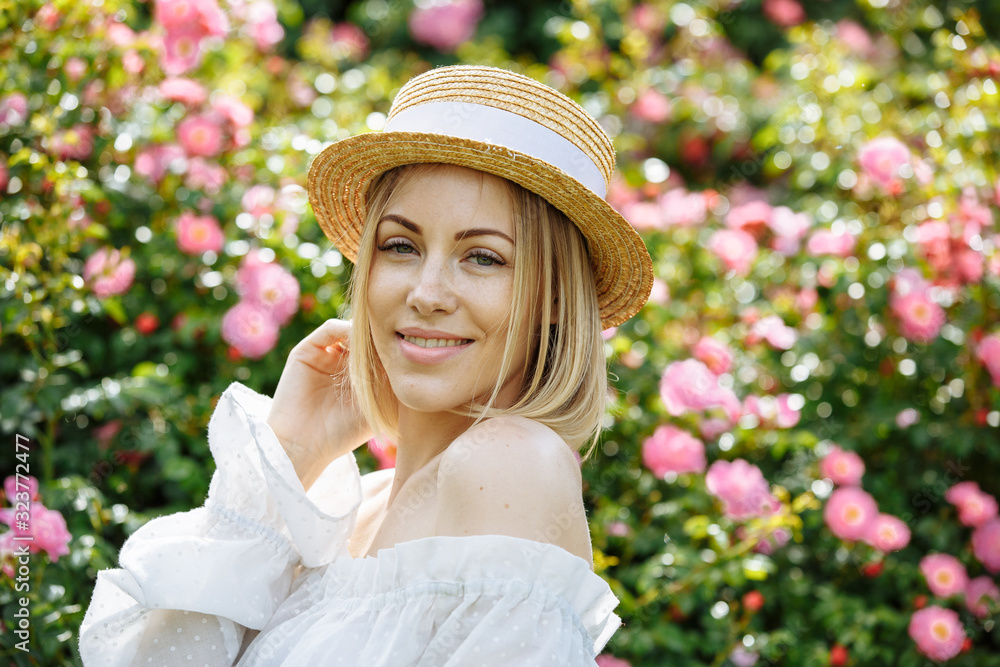 girl in a white dress with a hat in the garden with pink roses