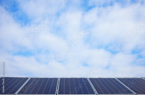Solar panels in a line on top of a roof with cloudy blue sky