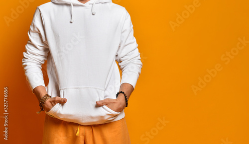 man in a white sweatshirt, pants and bracelets. Folded hands in pockets and posing on an orange background. Fashion and Style. Close copy space