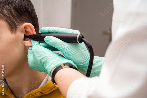 Preventive inspection of a teenage boy in a medical facility. Otorhinolaryngologist doctor pediatrician. Inspection of the sinuses of the ear with the reflector of the forehead and the nasal mirror photo