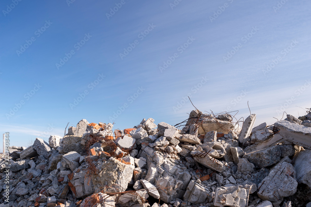 A pile of large gray concrete fragments with protruding fittings against a blue cloudy sky. Background.
