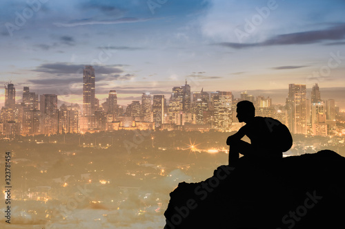 Young man sitting on a mountain overlooking city watching the sunset. 