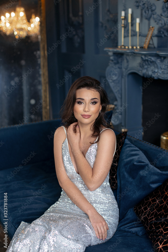 Beautiful romantic brunette in silver dress posing at sofa in royal interior Beautiful romantic brunette in silver dress posing at sofa in royal interior