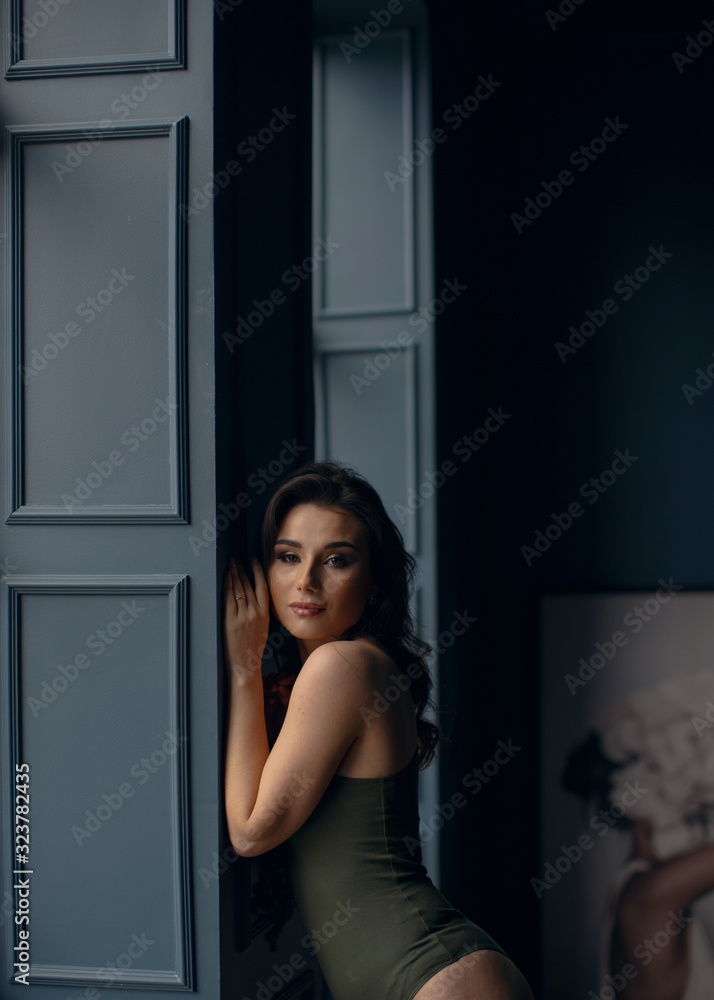 Fototapeta premium Young sexy girl in green bodysuit poses near the window.
