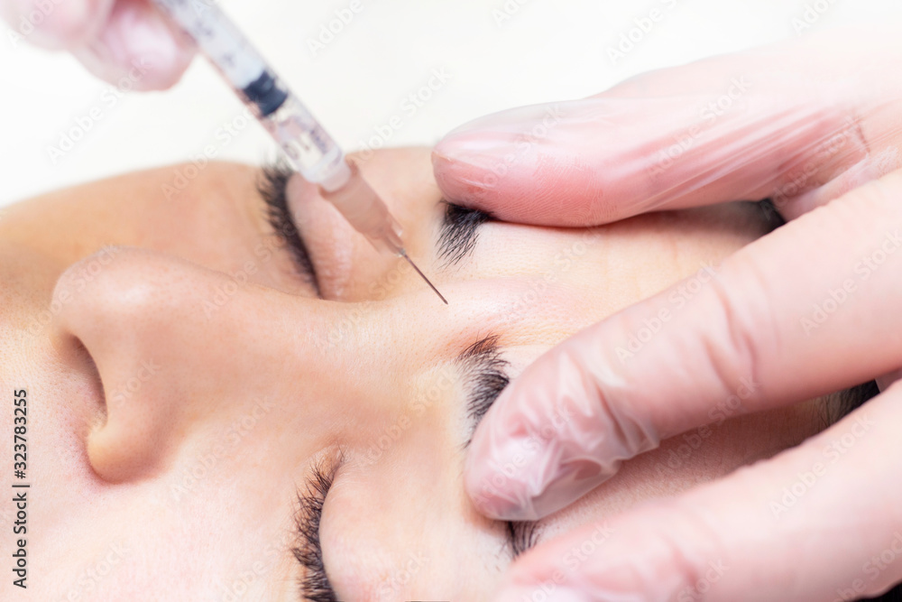Close-up of a beautician injecting Botox into forehead wrinkles. She holds a syringe. Botox injection. Cosmetics injected womans face Close-up of a beautician injecting Botox into forehead wrinkles. She holds a syringe. Botox injection. Cosmetics injected womans face