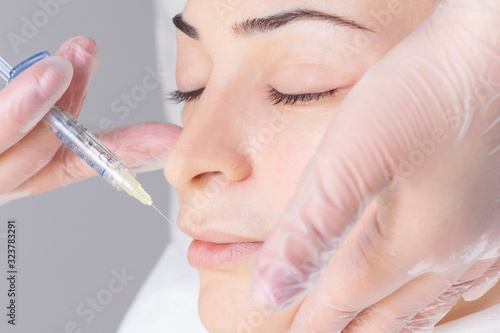 Close-up Of Beautician Injecting Botox On Female Lips. She holds a syringe. Young beautiful woman gets procedure with pleasure