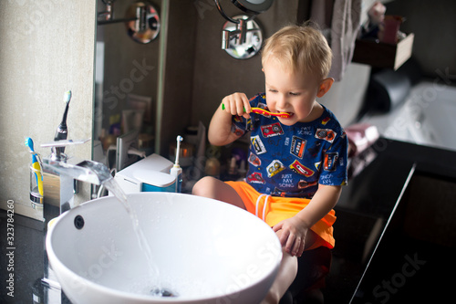 Little funny baby boy sitting in bathroom and brushing his teeth. Learning hygiene procedure