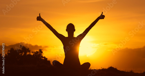 Young woman with thumbs up facing the sunset feeling happy and inspired. 