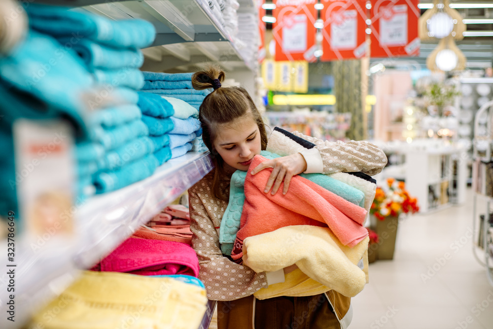 young woman shopping towels. A teenager picks a big towel on the shelves of a store. Multi-colored cotton fluffy. Homeliness