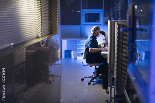 In a Modern Laboratory Scientist Conduct Experiments. Chief Research Scientist Adjusts Specimen in a Petri Dish and Looks on it Into Microscope.