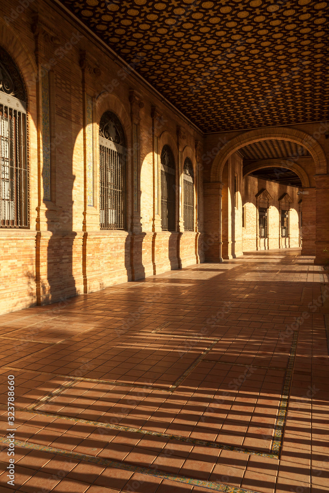 Details of the architecture and decoration in the corridor located in Plaza de España in Seville, under warm orange light at sunset.