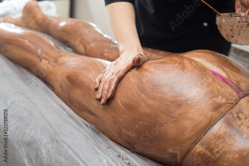 Massage therapist smears the females body with chocolate. Cosmetic procedure with chocolate for the body in the spa