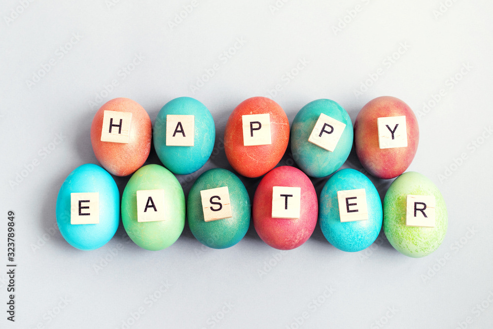 Text HAPPY EASTER made from wooden letters and bright multi-colored Easter eggs on a gray background, top view. Easter background. Text HAPPY EASTER made from wooden letters and bright multi-colored Easter eggs on a gray background, top view. Easter background.