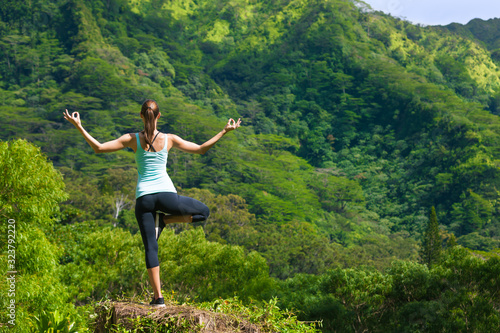 Female doing balancing meditation pose in a green mountain setting. 