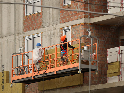 Φωτογραφία Two workers in a construction basket insulate the glassy wall of a multi-storey building