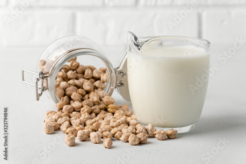 Dairy-free milk. Chickpea nut scattered on the surface in a glass jar and milk in a mug on a light background. Lactose free.