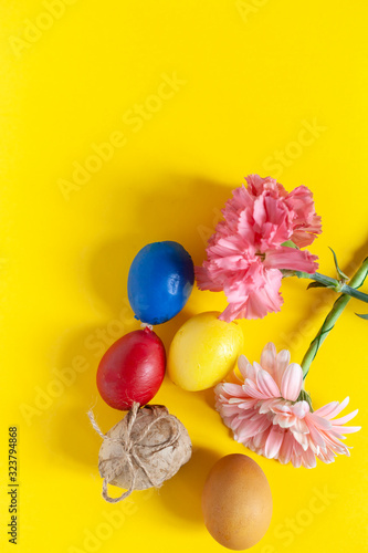 Colorful easter eggs with bright colorful spring flowers on the yellow background. Top view. View from directly above. Spring festive holidays background. Vertical image