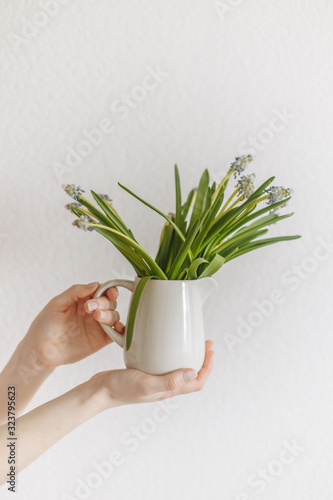 Female hands hold green flowers in a white ceramic vase white background