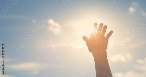 Hand reaching up touching the sun sunset sky with rays of light shinning through fingertips, 
