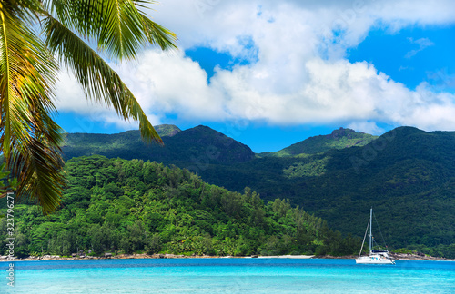 Beautiful seascape bay with luxury yacht at the coast,tropical island at background and palm tree leafs at foreground
