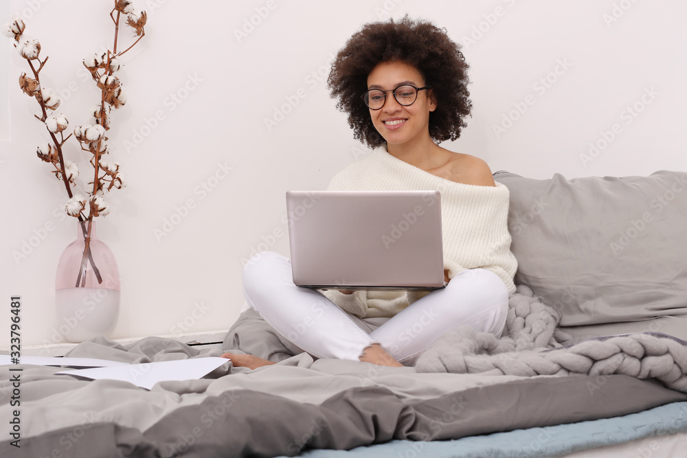 Happy casual beautiful woman working on a laptop, sitting on bed at home. Cozy , casual style Happy casual beautiful woman working on a laptop, sitting on bed at home. Cozy , casual style