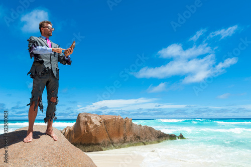 Fotografie Survivor businessman in tattered suit standing on rough rock using coconut husk