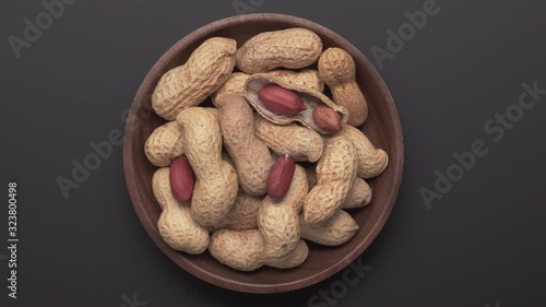 Bunch of peanuts in bowl rotating on dark gray background. Top view Close up. Arachis hypogaea photo