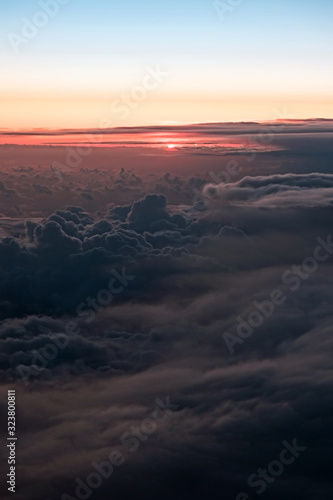 Sunset above clouds illuminated by the rays of the sun from airplane window. View of the beautiful cumulus clouds at sunset from an airplane window, true colors.