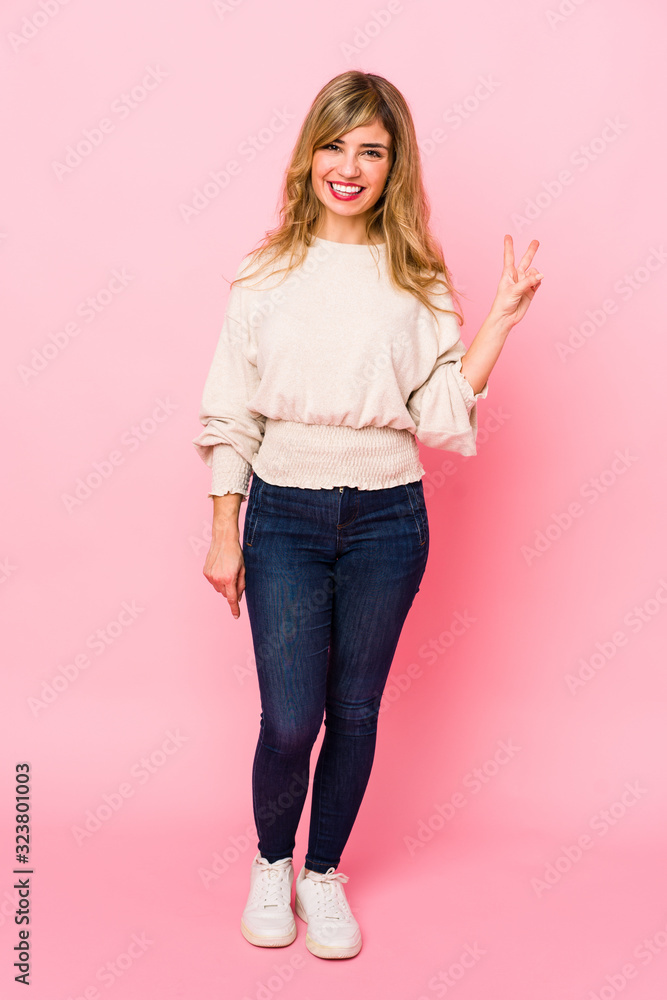Young blonde caucasian woman standing over a pink background showing victory sign and smiling broadly. Young blonde caucasian woman standing over a pink background showing victory sign and smiling broadly.