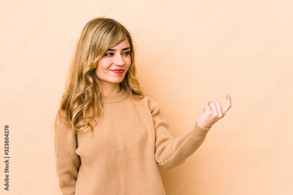 Young blonde caucasian woman pointing with finger at you as if inviting come closer. Young blonde caucasian woman pointing with finger at you as if inviting come closer.