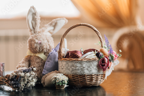 Easter basket with decorated eggs and plush bunny on wooden background.
