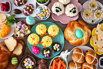Easter table scene with an assortment of breads, desserts and treats. Top view over a wood background. Spring holiday food concept.