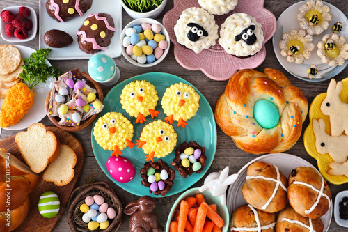 Easter table scene with an assortment of breads, desserts and treats. Top view over a wood background. Spring holiday food concept.