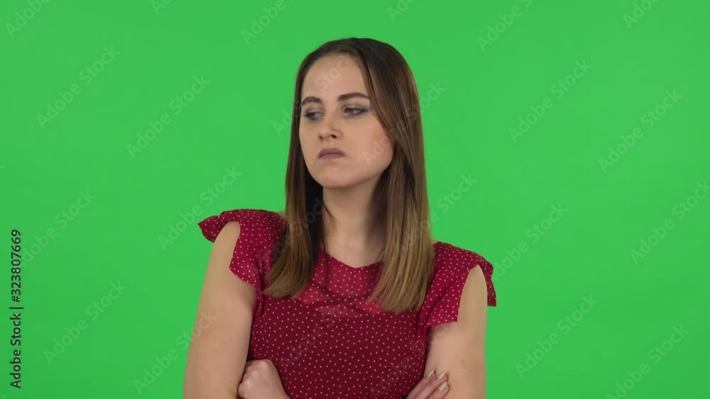 Portrait of tender girl in red dress is very offended and looking away. Green screen