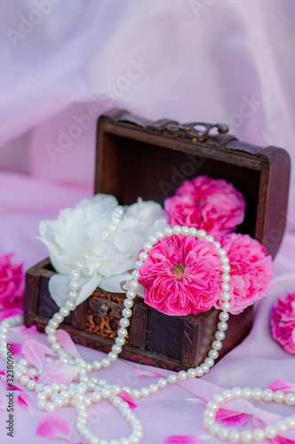 Floral arrangement of pink roses flowers and peonies in a wooden box with pearl beads on a pink background. Flat lay of wedding decorations and decorations. Floristically photo