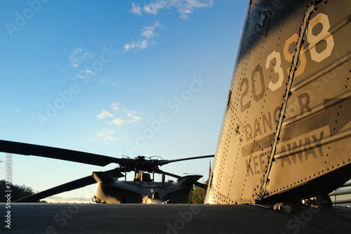 rear view of the tail of a military helicopter and main rotor propeller blades against a blue sky at sunset