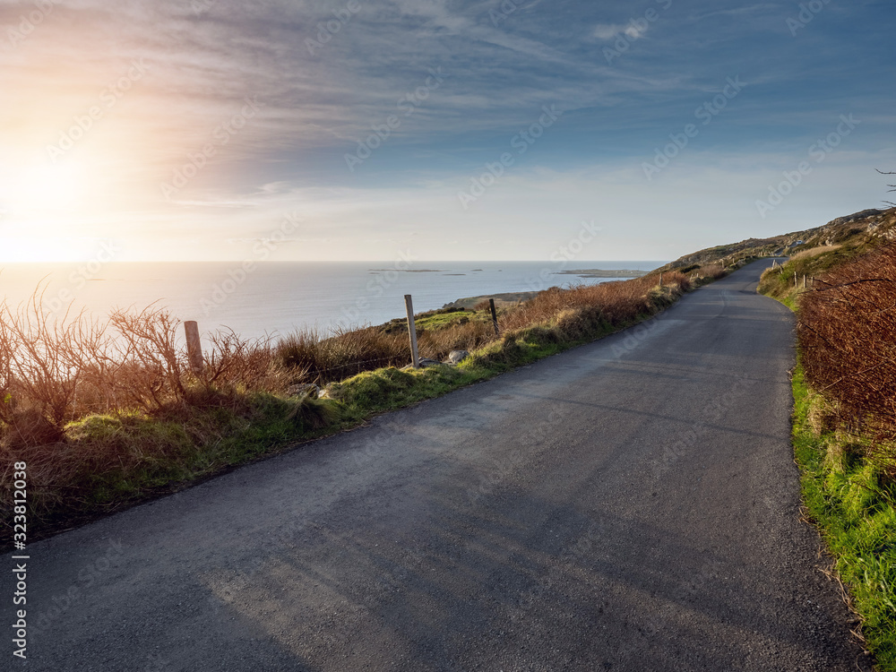 Fototapeta premium Road by ocean at sunset time. Calm blue sky. Nobody, West coast of Ireland.
