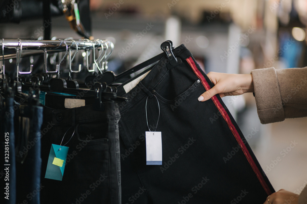 Close up of woman choosing jeans. Hand of female holding jeans in clothes store