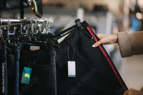 Close up of woman choosing jeans. Hand of female holding jeans in clothes store