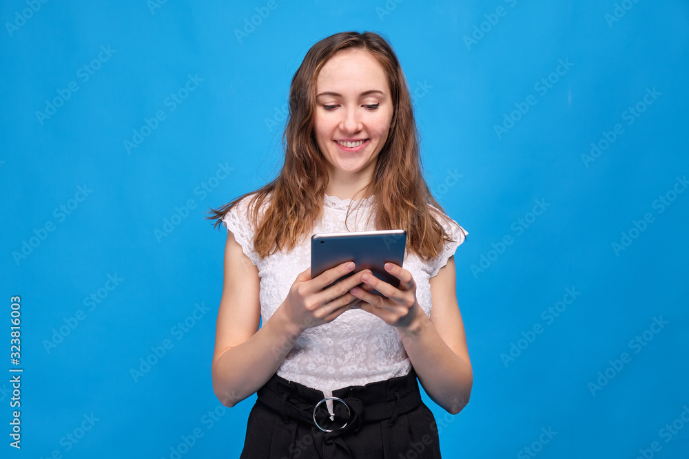 Brunette girl in casual clothes on a blue background and watching funny films, TV shows, shows through a tablet Brunette girl in casual clothes on a blue background and watching funny films, TV shows, shows through a tablet